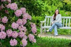 CEO Grace Elton sits on a bench with pink rhododendrons in bloom in the foreground.