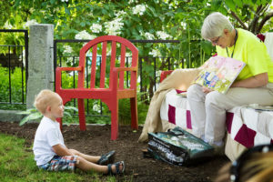 A child sits on the ground while being read a story in the garden.