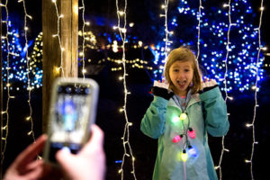 An evening image of a young girl posing for a photo next to multicolored lights.