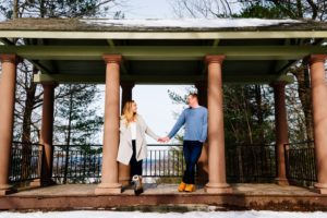 A couple stands against pillars holding hands.