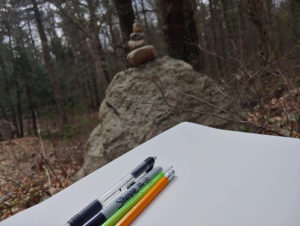 Drawing and writing supplies on a notebook outdoors.