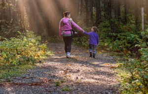 A mother and daughter walk hand in hand through the woods.