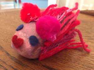 Pet rock painted pink with pom pots and yarn glued on