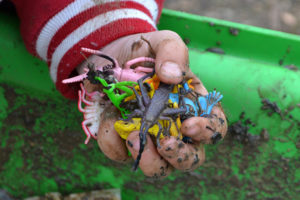 A child holds a handful of toys from a sensory bin.