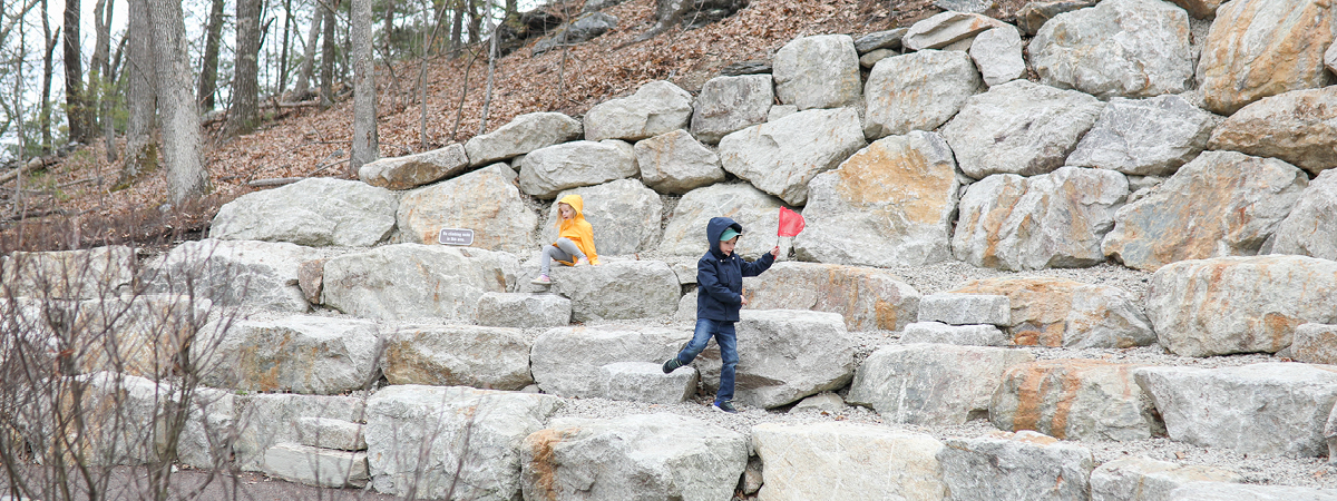 Two children run around the rock feature In the Ramble.