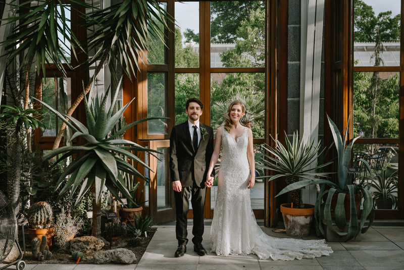 A wedding couple pose for a photo beside plants in the Orangerie.