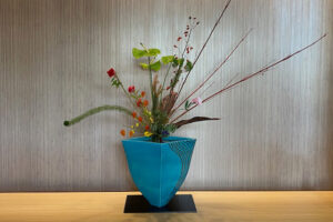 An ikebana display with a blue vase and interesting flowers.