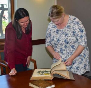 Grace Elton (left), CEO of the Garden and Elizabeth Slomba (right), University Archivist and Interim Special Collections Librarian at UNH examine botanical illustrations from the rare book collection.