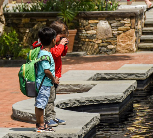 Two children stand next to the turtle pond in the Winter Garden using Discovery Backpacks.