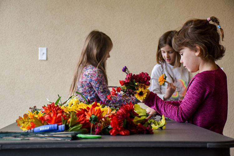 Three girls stand around a table with flowers making a craft during vacation week.
