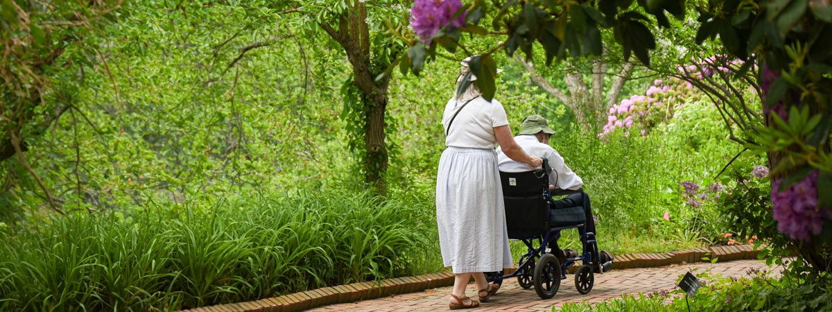 A visitor pushing someone in a wheelchair around the Lawn Garden.