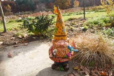 A gnome covered in painted bugs stands in the garden.