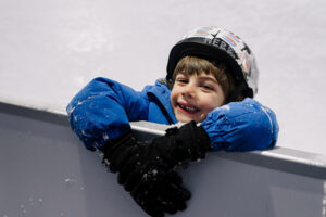 Kid smiling at Night Lights outdoor skating rink with a helmet on