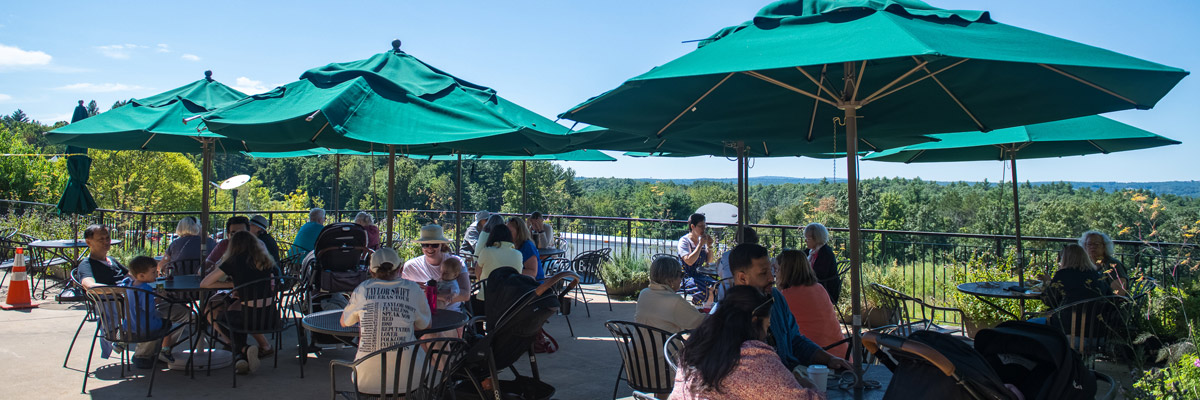 visitors dining outside on the terrace on a sunny day under large green umbrella tables