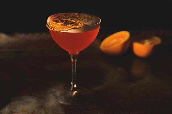 A drink with dehydrated orange slices set in a dark and smoky setting