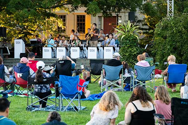 Visitors sitting on lawn chairs or sat on the Garden's lawn, watching the orchestral group, Beantown