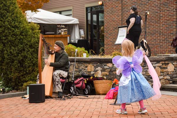 A child in a fairy costume watching a musician play the harp outside at the Garden