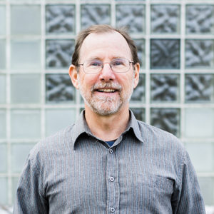 Jono Neiger smiles in front a gray building with clear glass tiles