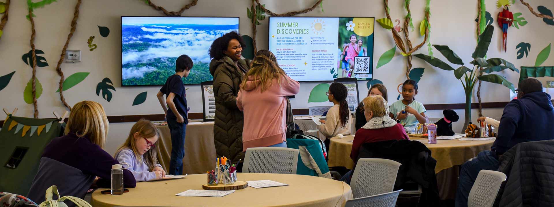 a group of parents and their children in a decorated classroom of paper leaves and vines