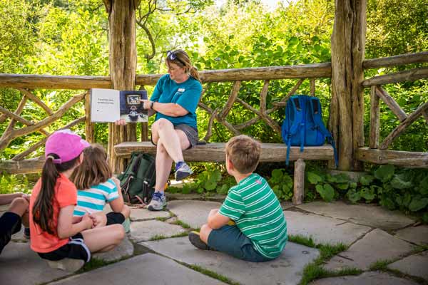 An instructor presenting and reading a book as children sits and listen outdoor at the Viewing Pavilion