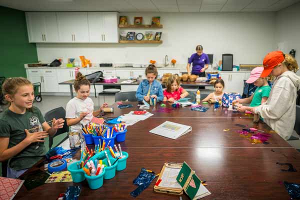 Kids and instructors surrounding a table full of art supplies