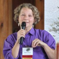 Speaker, Nadine Mazzola, in a purple button up shirt speaking into a black microphone that in her hand