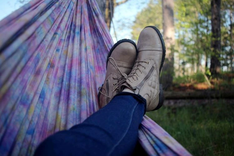 First-person perspective of a person feet worn with boots laying on a hammock outside with trees surrounded