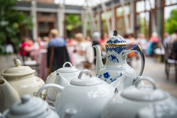 afternoon-tea-optimize ceramic white tea sets in focused with guests at table dining in a conservatory in the background