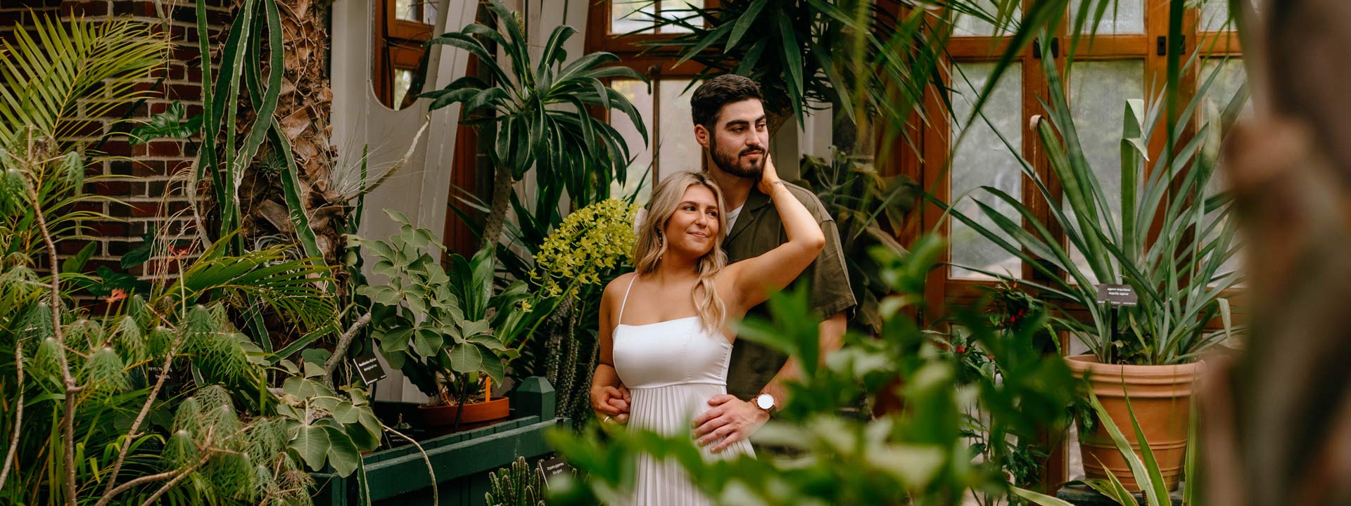 A couple posing for the engagement photoshoot in a lush green conservatory
