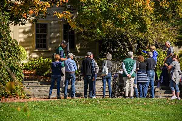 A group of people listening to a Garden guide on the steps outside of the Farm House