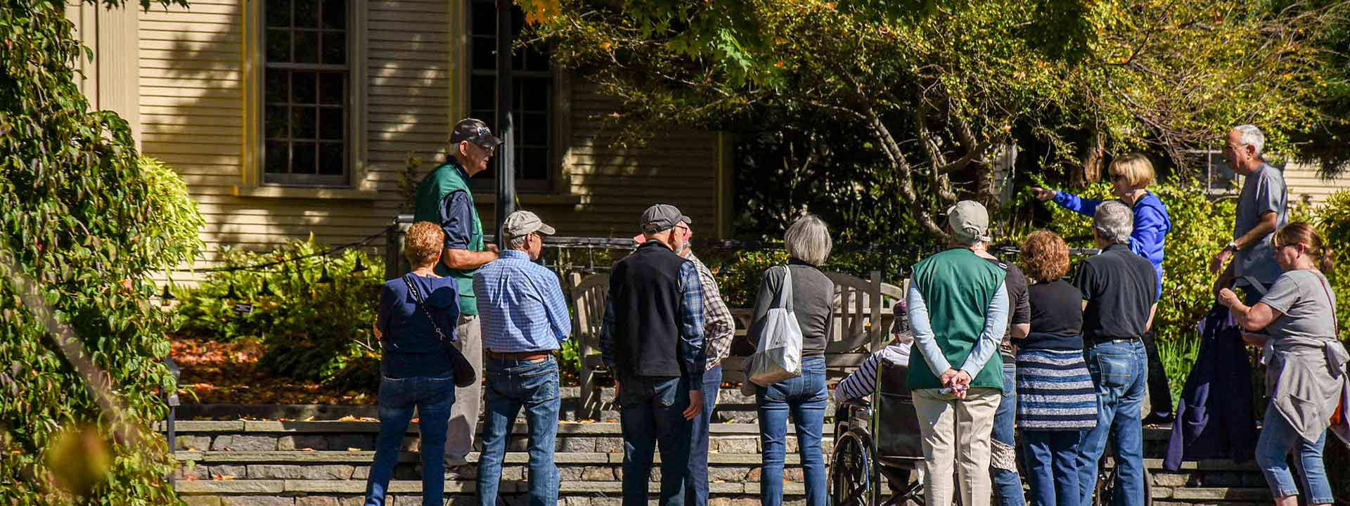 A group of people listening to a Garden guide on the steps outside of the Farm House