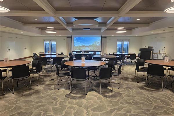 Round tables and chairs in the Reservoir room set up for a meeting with a projector screen