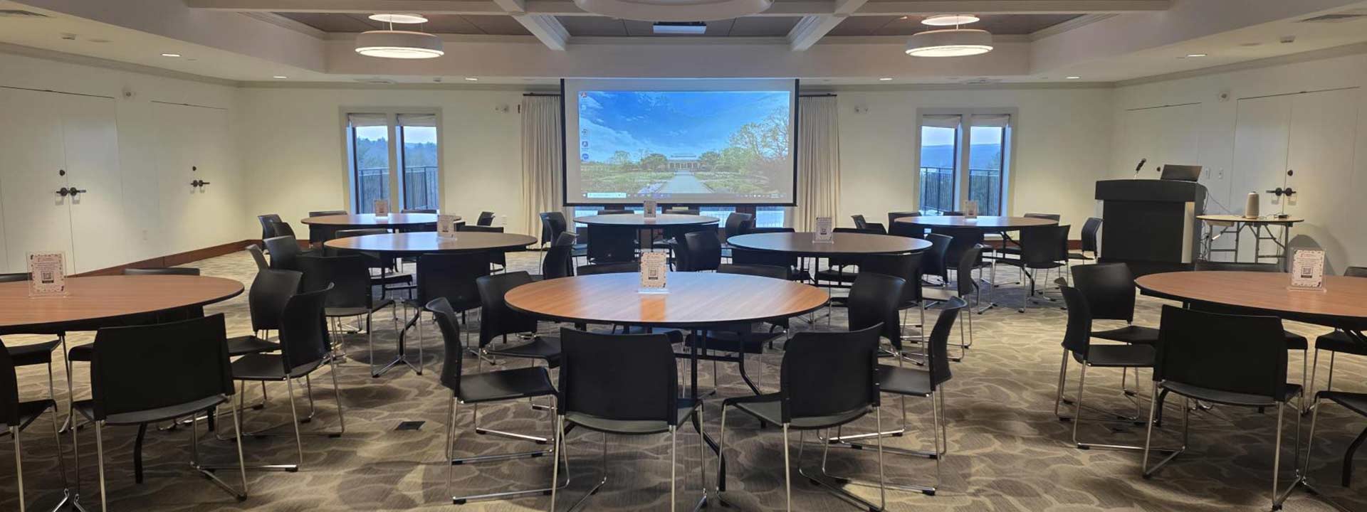 Round tables and chairs in the Reservoir room set up for a meeting with a projector screen