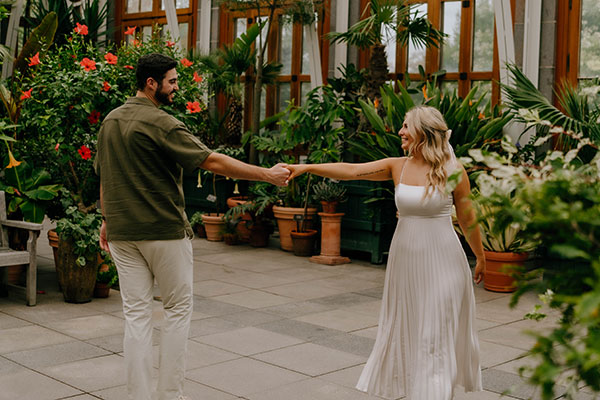 A couple reach for each other hands with arms stretched, romantically in the conservatory