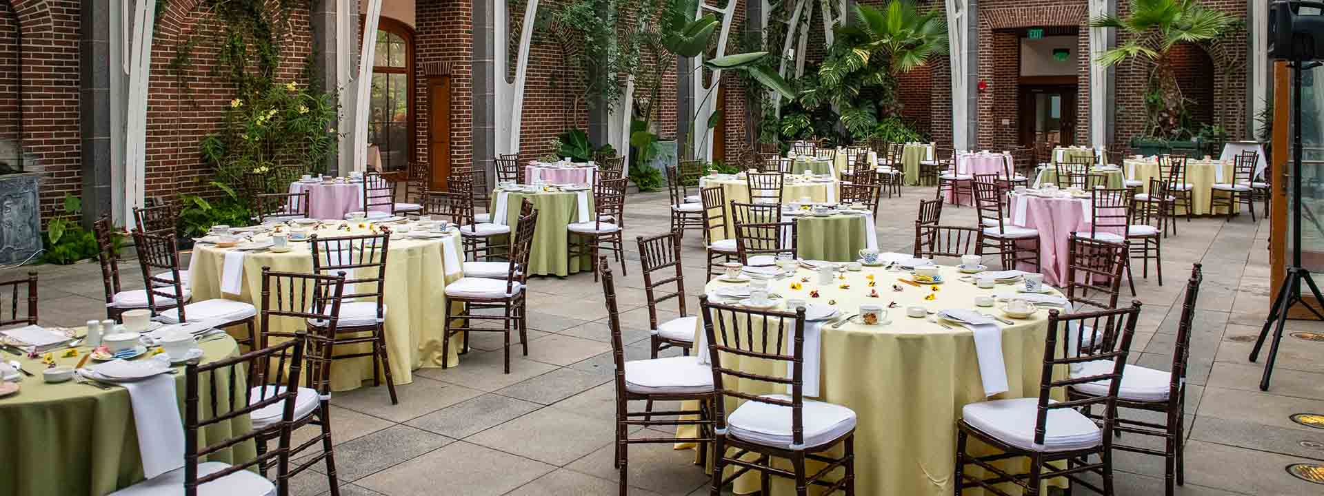 Fancy table and chairs in pastel yellow and mint green table cloths set up for a social event in the Oragerie