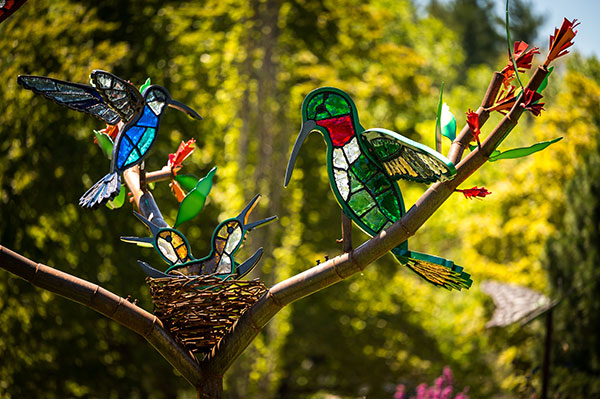 A larger-than-life glass sculpture of a family of birds in a steel nest and tree